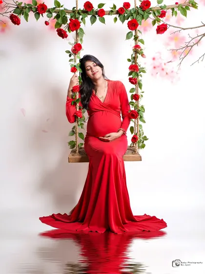 A beautiful solo shot on a floral swing with a water reflection effect. The mom-to-be's red gown stands out against the simple background, creating a striking image.