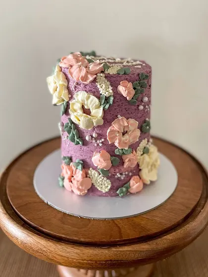 This tall barrel cake is a great example of my floral buttercream work. The textured purple frosting is adorned with hand-piped flowers in pastel pinks and yellows, creating a beautiful garden effect.