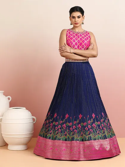 A striking navy blue pleated silk lehenga with a rising floral motif, paired with a vibrant pink embroidered blouse. The color contrast is bold and beautiful.