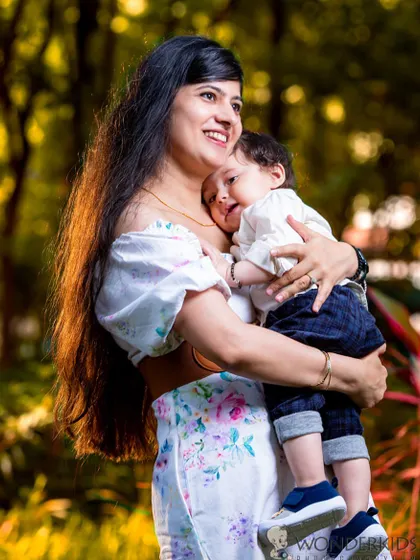 A mother holds her baby boy close, both smiling happily in a sunlit park. This photo captures the warmth and love of a mother's embrace in a natural, beautiful setting.