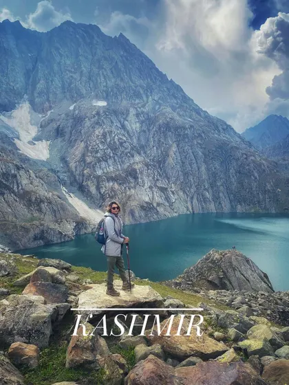 A trekker posing in front of a stunning alpine lake in Kashmir. Our trips go beyond the usual tourist spots to show you the real beauty of the region.