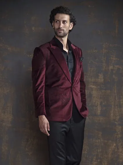 A full-length view of the maroon velvet blazer. Paired with black trousers, it creates a powerful and elegant statement for any formal event.
