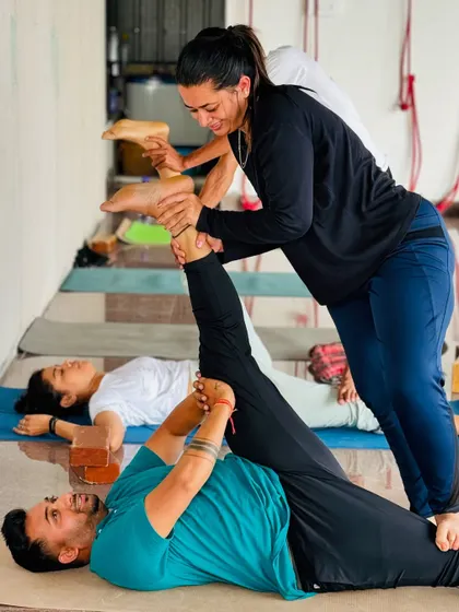 Hands-on adjustments are a key part of our teaching. Here, an instructor helps a student with a supine hamstring stretch, ensuring proper alignment and a safe, effective release.