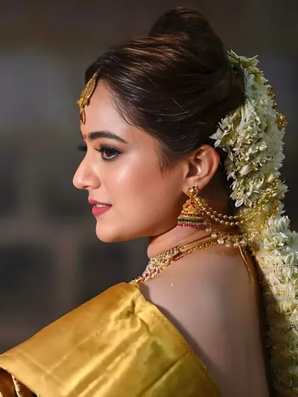 A beautiful side profile showcasing a traditional South Indian bridal look. The intricate hairstyle adorned with fresh flowers, known as gajra, and the classic gold jhumkas complete this elegant wedding day makeup.