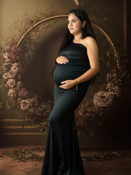 A classic maternity pose in a black gown, with the mom-to-be framed by a dark floral hoop for a touch of romantic drama.