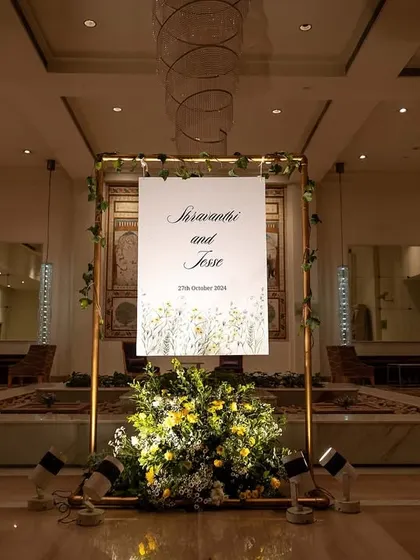 An elegant and modern welcome sign in a grand hotel lobby, framed in gold and accented with simple greenery.