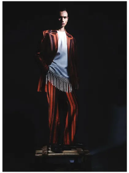 The model stands on a wooden pallet, illuminated by a single, harsh light source that casts deep shadows. This image from the 'Silhouette' series showcases a raw, industrial edge within a high-fashion context.