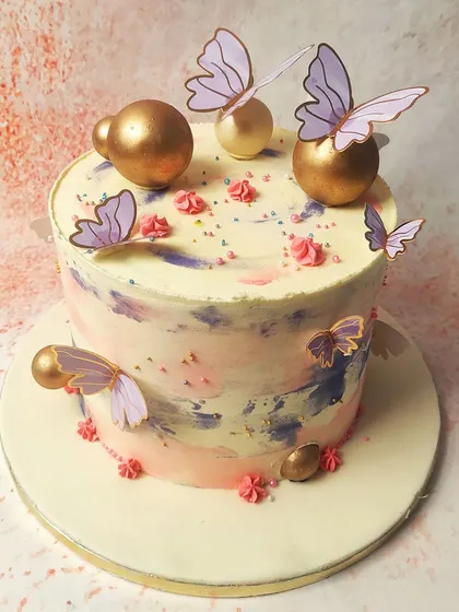 We paint with pastels on this abstract butterfly cake. A watercolor-like blend of pink, purple, and blue buttercream creates a dreamy canvas for delicate purple and gold butterflies and shimmering gold spheres, resulting in a piece of edible art.