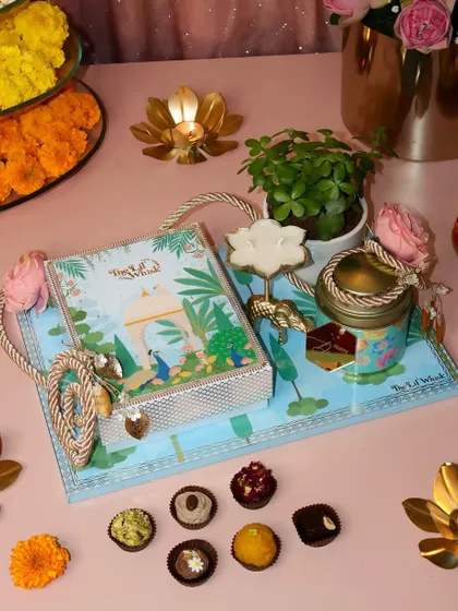 Our Gardenia Platter is a gift of indulgence and nature. It features a box of 12 assorted sweets, dry fruits, a candle, and a beautiful jade plant, all arranged on a reusable tray.