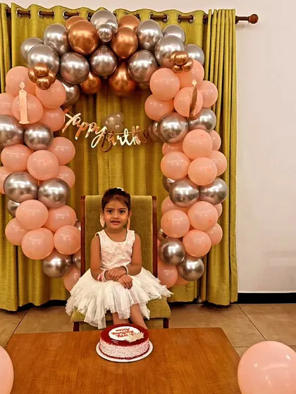 This simple and sweet home birthday setup features a balloon arch in pastel peach and chrome silver. It creates a lovely, intimate backdrop for capturing memories, as seen here with the birthday girl ready to cut her cake.