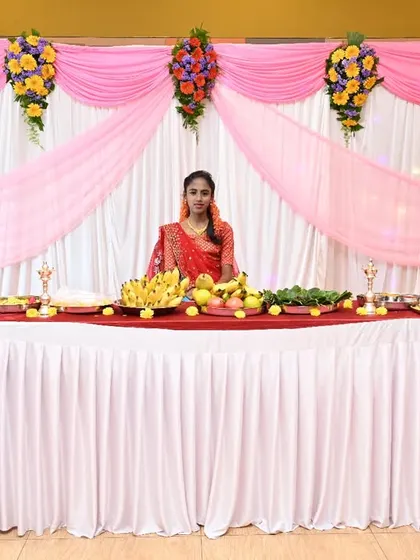 An elegant stage for a half-saree ceremony. The backdrop uses simple white and pink drapes, accented with colorful floral bouquets on pillars, creating a graceful setting.