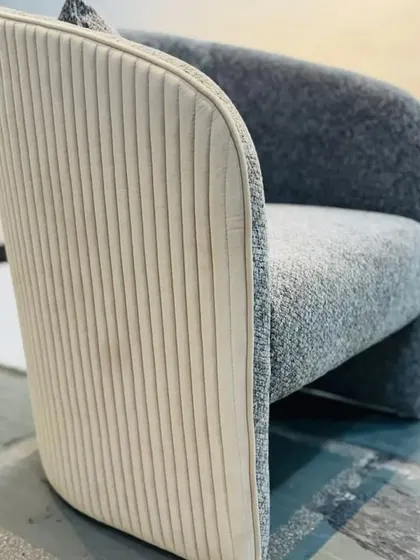 A detail shot of a modern armchair, showing the contrast between the textured grey fabric and the vertically stitched cream leather on the back. This highlights our focus on combining materials for a unique finish.