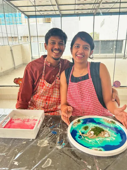 A couple with their finished resin art pieces, one a beach scene and the other a fluid art tray.