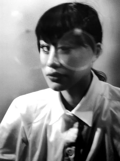 An intense close-up black and white portrait on film, with lens flare or a reflection creating a circular artifact over the model's face. This imperfection adds a unique, artistic character to the shot.