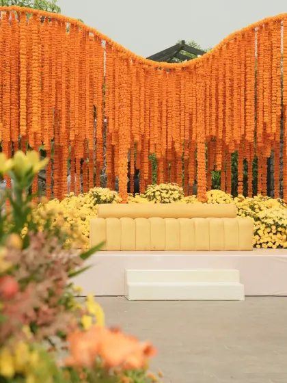 The main stage for a Haldi ceremony, with a flowing curtain of orange marigolds creating a stunning and traditional backdrop.