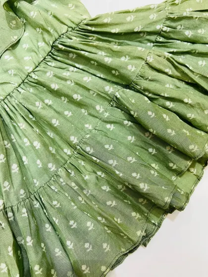 A close-up of the tiered ruffles on our green cotton summer dress. The gathered layers add volume and movement, making it a fun dress for your child to wear.