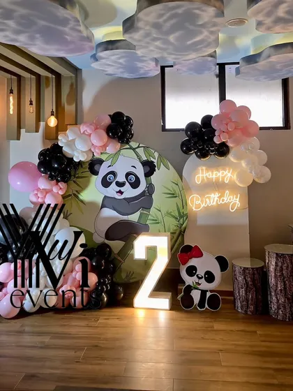 A cute panda-themed second birthday party setup, with a custom backdrop, black, white, and pink balloons, and a light-up number '2'.