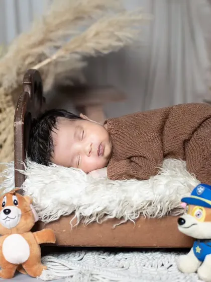 This newborn is sleeping on a miniature bed, surrounded by cute Paw Patrol and Tom and Jerry toys.