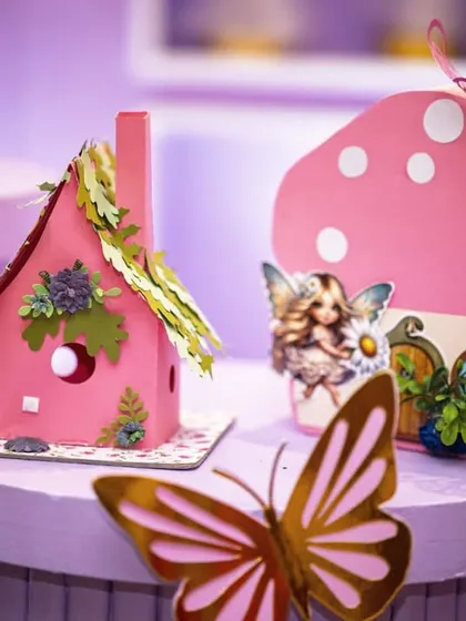 A close-up of the handcrafted props for a fairy garden party, including a miniature house with a leafy roof and a pink mushroom house. These details help build an immersive, magical atmosphere.