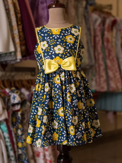 A cheerful navy blue dress covered in a bright yellow and white floral print. The large yellow bow at the waist makes this a sunny and happy choice for any day.