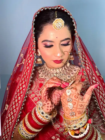 A close-up on the details. This image focuses on the bride's intricate henna, her beautiful red lehenga, and the soft, shimmery eye makeup with a classic red lip.