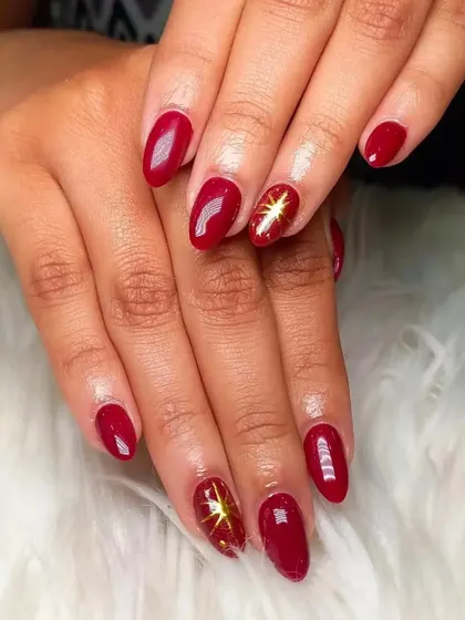 A simple yet striking design with glossy red nails and a single accent nail on each hand featuring a gold starburst.