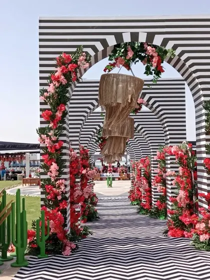 Symmetry, pattern, and blooms. This stunning entrance for a Doha celebration features a tunnel of black-and-white striped arches, lined with vibrant red flowers and quirky cactus props.
