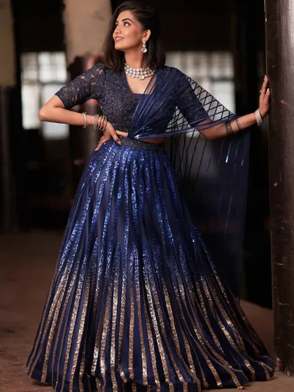 This contemporary lehenga set plays with light and texture. The dual-toned panel skirt creates a beautiful ombre effect, paired with a blouse featuring geometric cut dana details and a structured stripe dupatta.