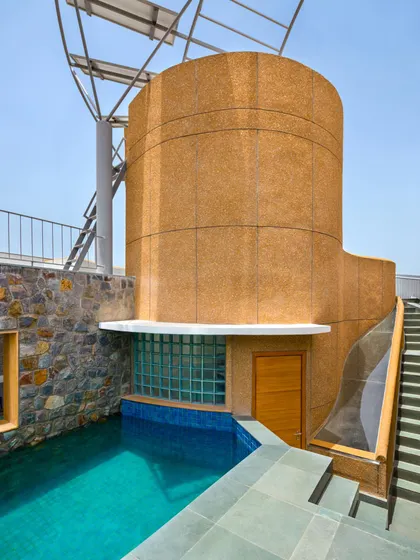 The rooftop splash pool is nestled beside the central cylindrical core, which is finished with a textured stone-grit plaster. This area is designed for relaxation and serves as the starting point for the home's rainwater harvesting system, showcasing the integration of leisure and sustainability.
