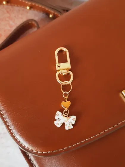 A simpler custom bag charm, featuring a white and gold polka dot bow and a small heart. It's chic and understated.