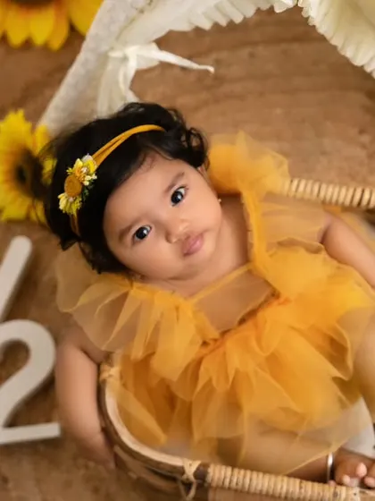 A bright and cheerful sunflower-themed six-month milestone shoot. The yellow dress and fresh flowers create a sunny and happy vibe.