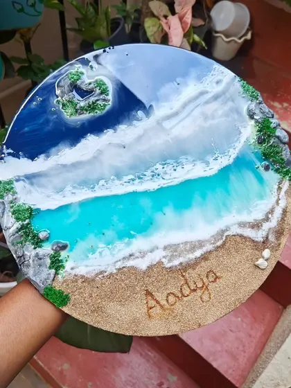 A finished personalized resin nameplate for 'Aadya'. This piece features a heart-shaped island and gentle waves on a round wooden base, capturing a peaceful beach scene.