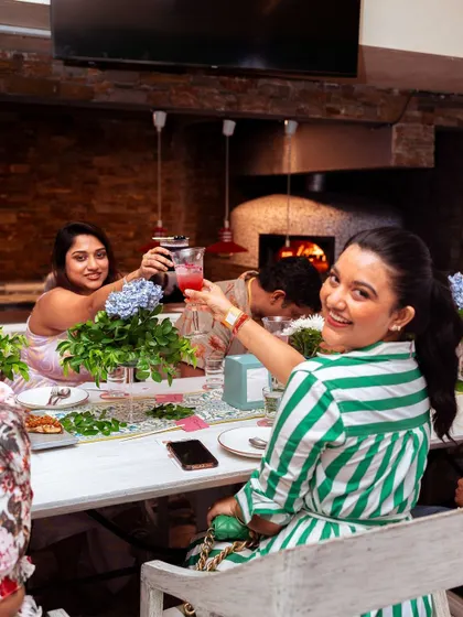 Cheers to a great meal! Guests at a long table celebrate together, with our wood-fired oven visible in the background, adding to the authentic culinary atmosphere.