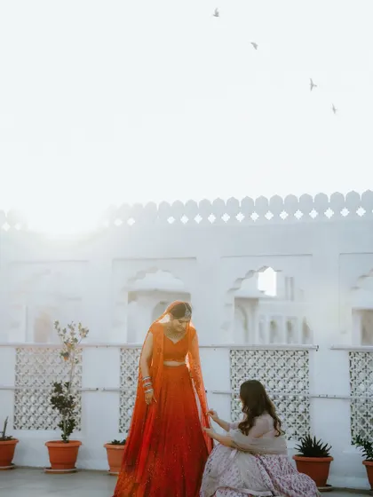 A sweet moment between the bride and her bridesmaid, set against a bright, minimalist background, with birds flying overhead, adding a touch of serendipity.