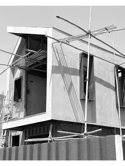 The structure takes shape with scaffolding in place. The original container is now integrated into a larger architectural form with a distinct cantilevered element.
