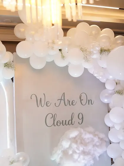 A close-up of the 'We Are On Cloud 9' sign, showing the delicate baby's breath flowers tucked into the balloon arch.