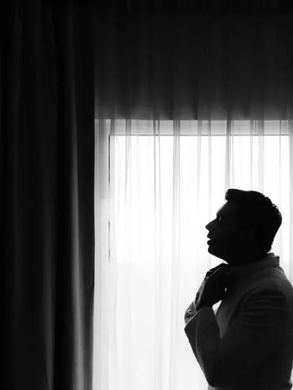 A dramatic black and white silhouette of the groom. This portrait, taken against a window, is a moment of calm and anticipation before the wedding festivities.