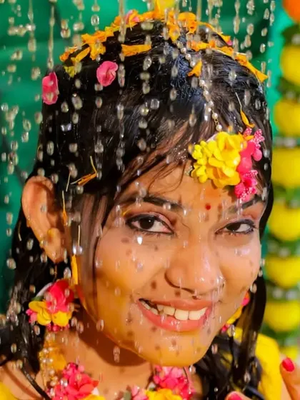 A close-up of a bride during her Haldi ceremony, smiling as she is showered with water and flowers. These candid shots are all about capturing genuine emotion.