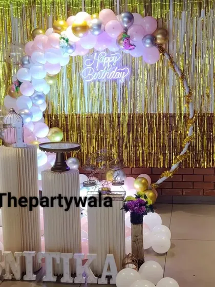 A ring decoration with a gold shimmer backdrop and pink, white, and silver balloons.