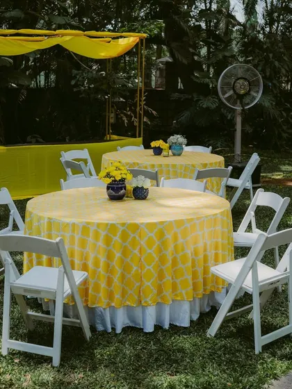 Guest seating at a Haldi ceremony, with tables covered in yellow patterned tablecloths.