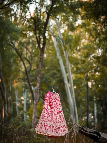 An artistic shot of the bridal lehenga displayed on a mannequin in a forest, contrasting the rich fabric with the natural environment.