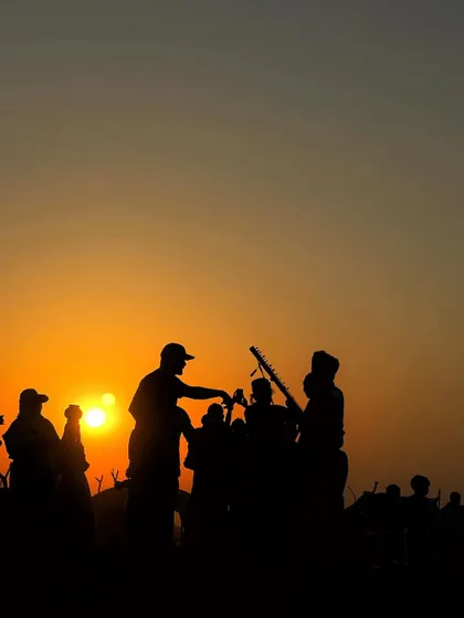 A silhouette of musicians and people gathered at sunset during the Pushkar Fair, creating a magical, atmospheric scene.