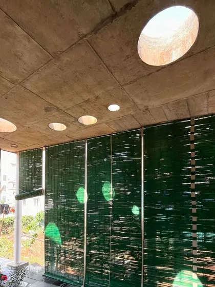 In this studio space, circular skylights punctuate the concrete ceiling, casting moving pools of light throughout the day. The green bamboo blinds offer a soft, diffused light and a connection to the natural world.