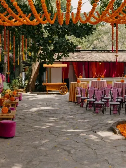 A wide view of the Haldi event space, showing the guest seating, lounge areas, and the canopy of hanging marigold strings.