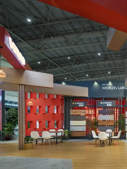 This 220 sq.m exhibition space for Virgo features a striking interplay of materials and volumes. A vibrant red lattice wall serves as a focal point, complemented by wood-clad structures and defined seating areas for visitor discussions.