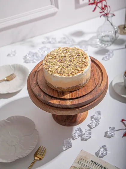 A pistachio-topped ice cream cake on a tiered wooden stand, surrounded by ice cubes to highlight its cool, refreshing nature.