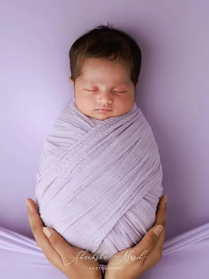 So small and precious. This classic swaddle pose, held gently in loving hands, emphasizes the baby's tininess and the protective love that surrounds them. The lavender tones add a soft, dreamy quality.