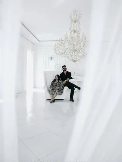 A creative, framed shot of the couple in the all-white room, viewed through a sheer curtain, adding a layer of softness.