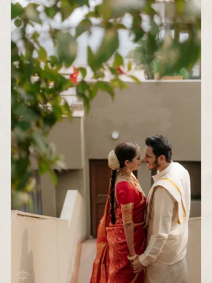 An intimate, artistic portrait of a couple in traditional South Indian wedding attire, framed by natural elements.