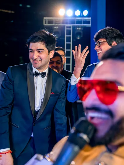 A candid shot of the groom's reaction during the Sangeet performances, surrounded by his laughing friends.